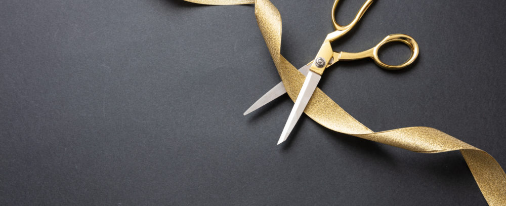 Grand opening. Gold scissors cutting gold satin ribbon, black background