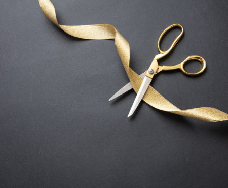 Grand opening. Gold scissors cutting gold satin ribbon, black background